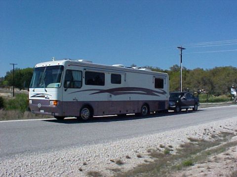 2002 Ford Supercrew - An RV is seen towing a pickup truck on a road under a clear blue sky.
