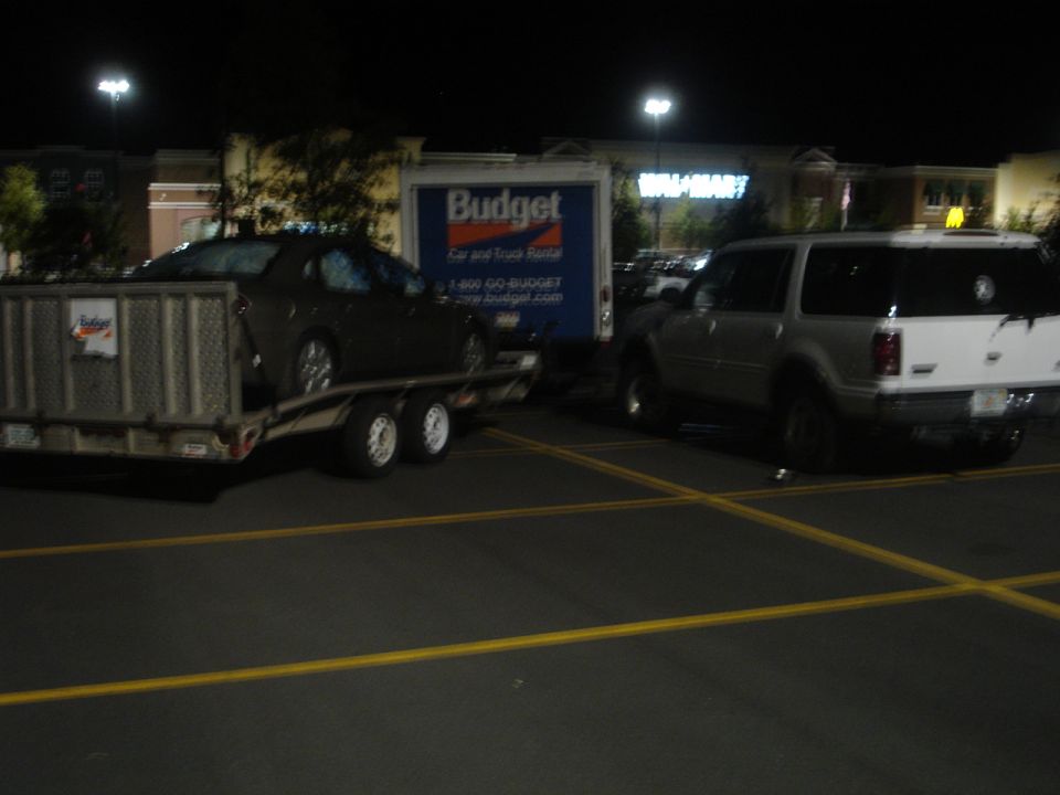 Silver SUV parked next to a Budget rental truck, with a car on a trailer in front of the truck