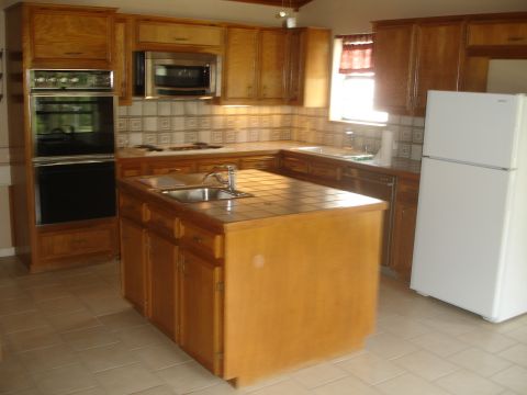 1989 Ford Bronco - Interior view of a kitchen wood cabinetry, a central island with a sink, and a white refrigerator.