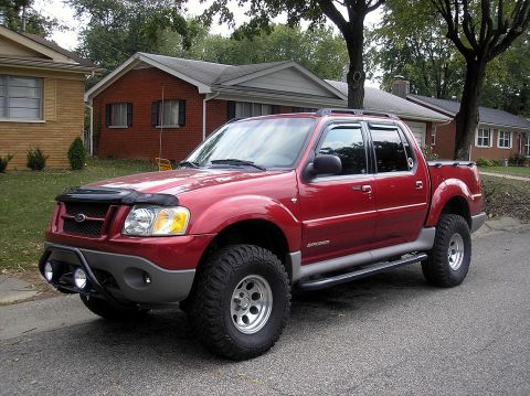 2002 Ford Sport Trac - Red Ford Explorer Sport Trac pickup truck with aftermarket modifications parked on a residential street.