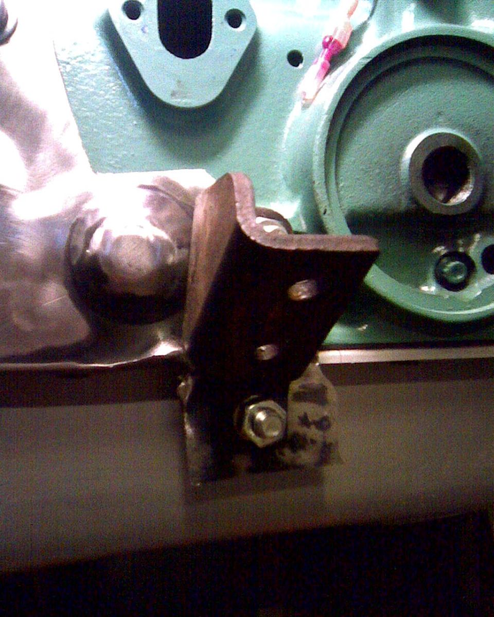 Metal bracket bolted to green engine block with visible bolt heads and a circular flange