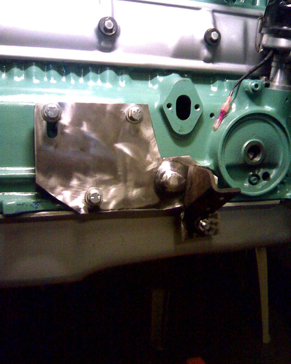 Engine block with a metal plate bolted on, showing a bracket and oil filter housing
