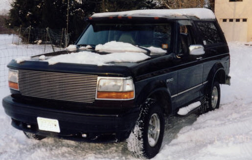Dark blue full-size Bronco SUV with billet grille parked in snow by a garage