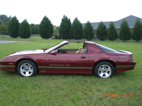 1979 Chevrolet Camaro - Maroon Chevrolet Camaro IROC-Z t-top parked on grass with trees and a building in the background.