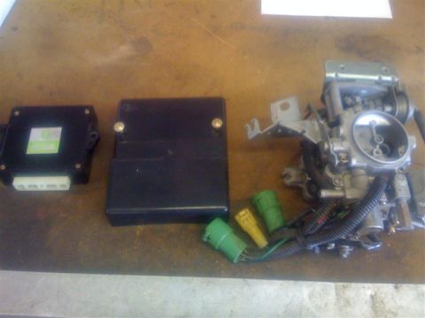 1994 Ford Bronco - Automotive parts including a carburetor and electronic control units are laid out on a workbench.