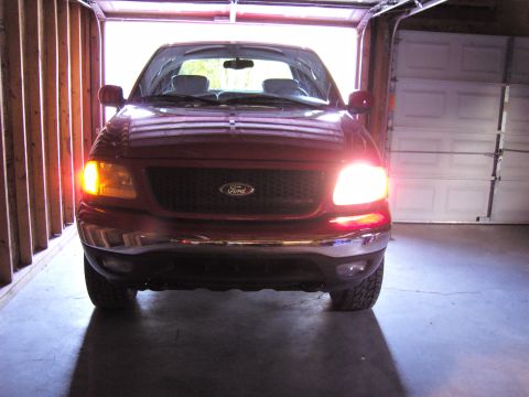 2007 Ford Mustang - The front grille and headlights of a red Ford F-150 are visible as it sits in a garage.