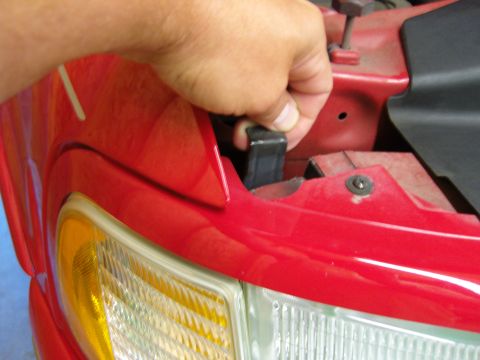 2007 Ford Mustang - A hand is shown removing a black clip from the headlight assembly of a red vehicle.
