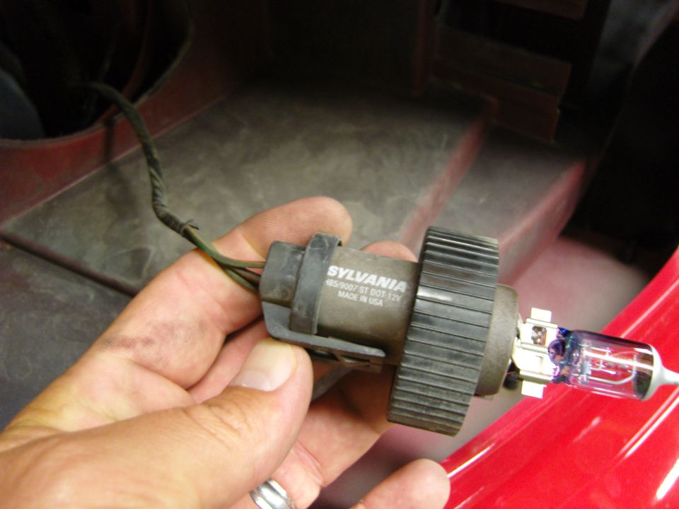 Hand holding a Sylvania headlight bulb assembly with part number 465607 ST DOT 12V