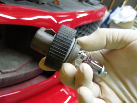 2007 Ford Mustang - A headlight bulb is held by gloved hands in front of a red car's grille, suggesting a repair or replacement.