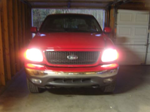 2007 Ford Mustang - This red Ford F-150 truck is parked inside a garage with its headlights illuminated.