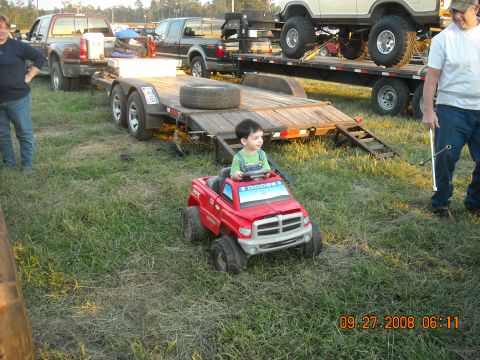 1979 Ford Bronco - A child drives a red toy Dodge truck in a grassy area with other vehicles and trailers in the background.