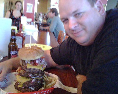 1989 Ford Bronco - Man poses with a massive triple-patty cheeseburger and fries at a restaurant.