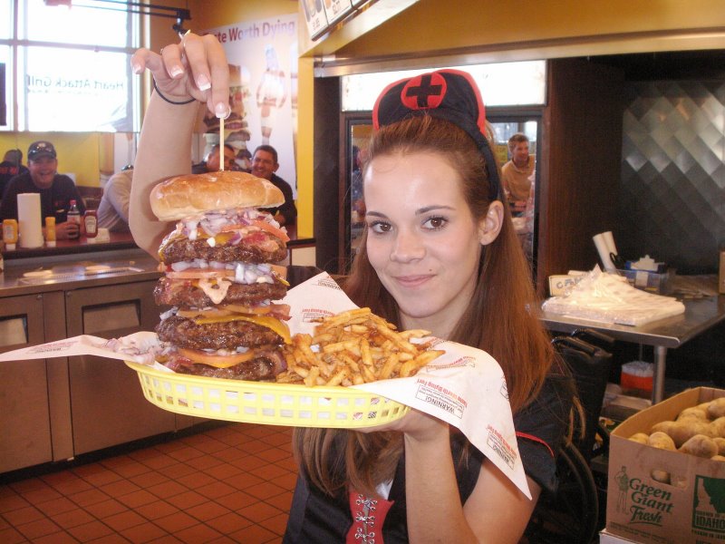 Woman in nurse costume holding a massive burger with four patties and fries