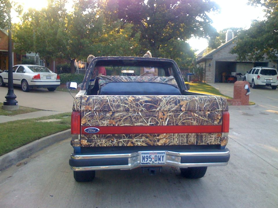 Rear view of camouflage-wrapped Ford Bronco with top removed, Texas plate M95-DWY, on suburban street