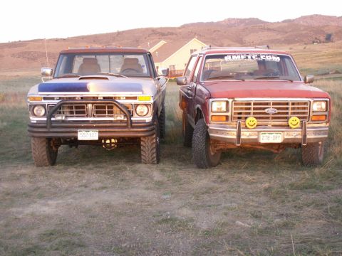 1977 Ford F-250 - Two Ford trucks are parked side-by-side, viewed from the front in an outdoor setting with hills in the background.