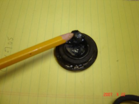 1993 Ford Bronco - A black rubber grommet is shown with a pencil tip touching it on a yellow lined background.