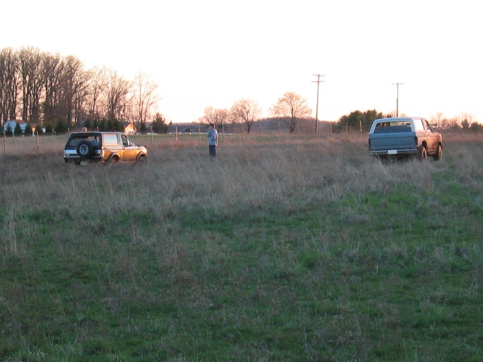 Two trucks and a person parked in a dry grass field at dusk