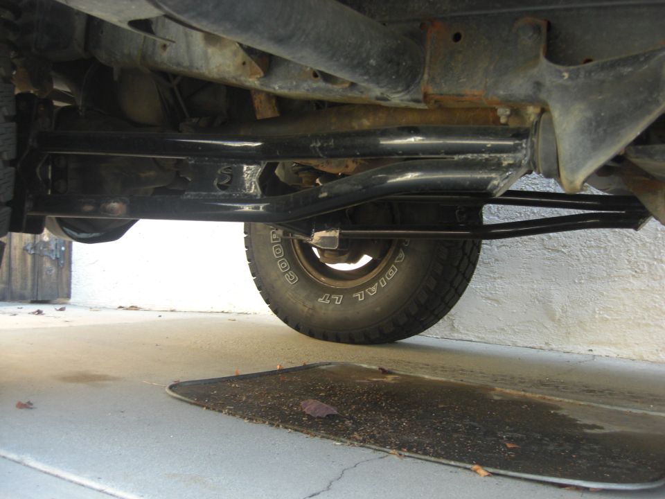 Underside view of a vehicle's frame, suspension, and tire. Shows rust on the frame and a Goodyear tire
