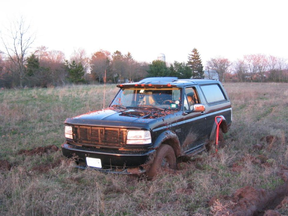 Black Ford Bronco stuck in a muddy field at dusk with tow strap