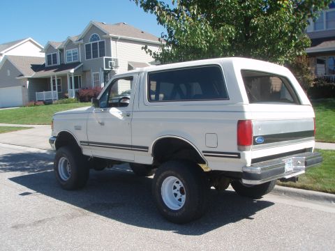 1987 Ford Bronco - A lifted white 1987 Ford Bronco is parked on a residential street with houses in the background.