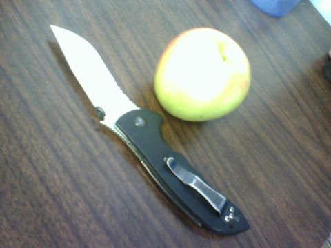 1984 Ford Bronco - A folding knife and an apple are placed on a wooden table. The image has a SUPERMOTORS watermark.