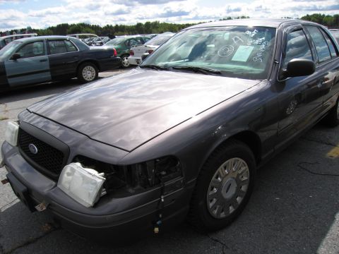 1991 Ford LTD Crown Victoria - A dark gray Ford Crown Victoria is parked in a lot, missing a headlight and showing some damage.