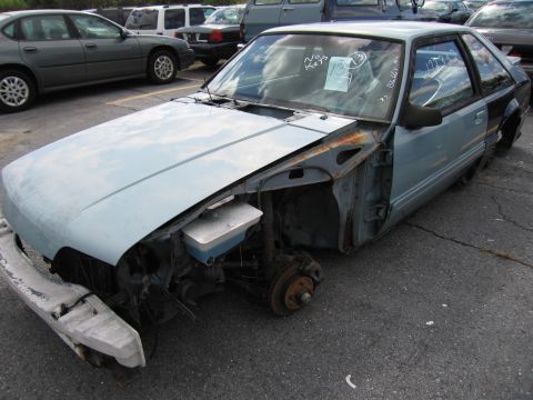 1991 Ford LTD Crown Victoria - A damaged light blue coupe sits in a parking lot with other vehicles in the background.