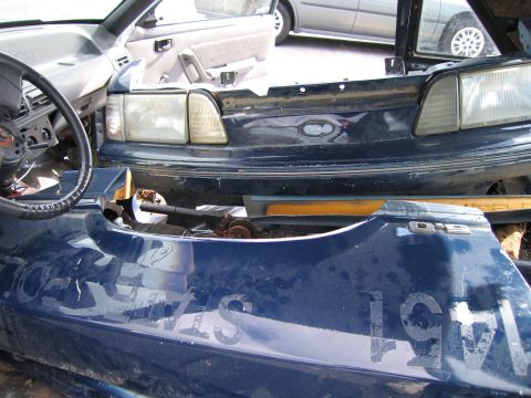 1991 Ford LTD Crown Victoria - A blue Ford Mustang fender with D15 badging and faded lettering is visible in a junkyard.