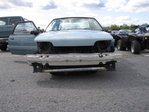 1991 Ford LTD Crown Victoria - Front view of a light blue sedan with its bumper and headlights removed, parked outdoors with other vehicles in a lot.