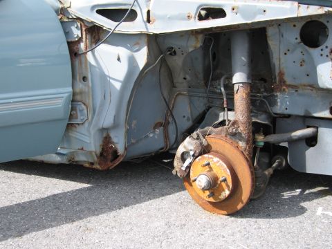 1991 Ford LTD Crown Victoria - Close-up of a heavily rusted car suspension system and fender section.