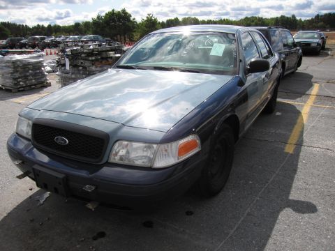 1991 Ford LTD Crown Victoria - A dark blue and gray Ford Crown Victoria is parked in a lot with other vehicles and stacked items.