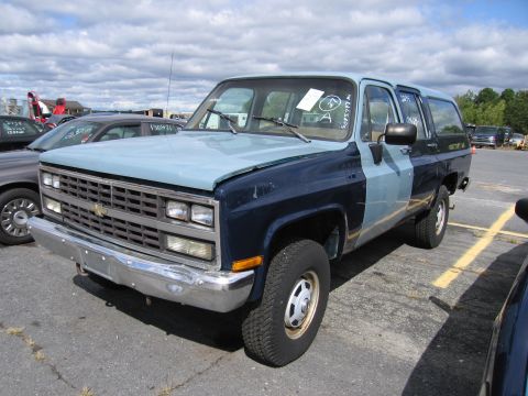 1991 Ford LTD Crown Victoria - A two-tone blue Chevrolet Suburban is parked in an outdoor lot with other vehicles.