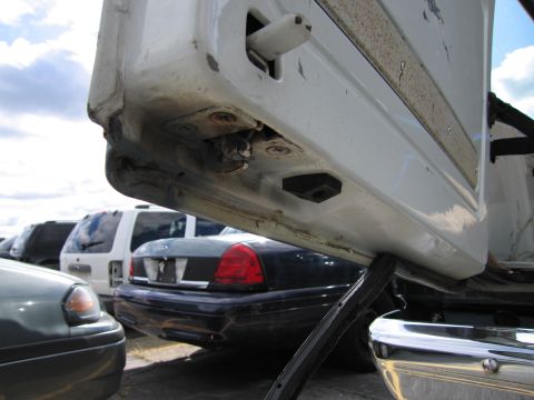 1991 Ford LTD Crown Victoria - The rear of a dark sedan is visible behind a white door frame in a junkyard.