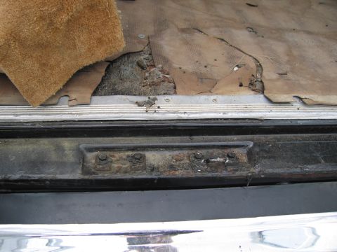 1991 Ford LTD Crown Victoria - The interior carpet is torn, revealing rust and damage to the underlying structure and latch mechanism.