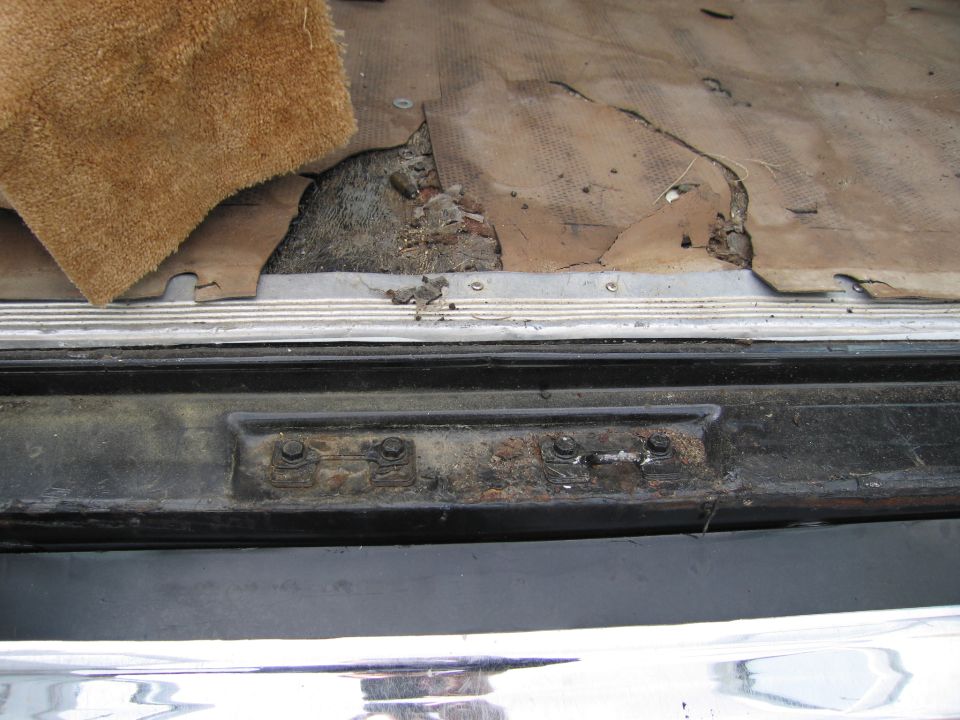 Torn carpet and rusted latch mechanism in a vehicle's trunk area