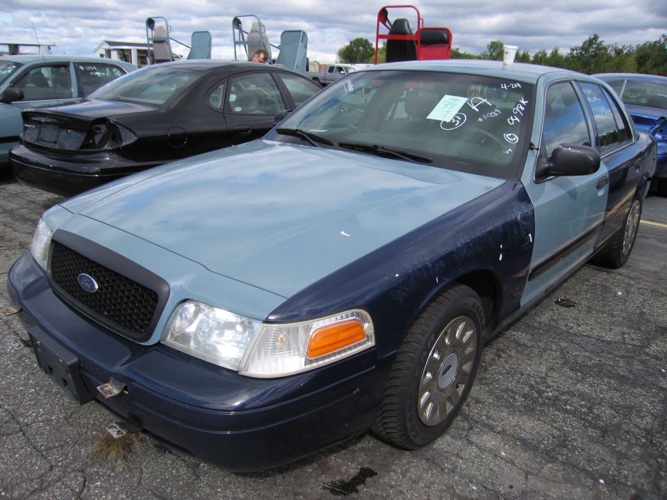 Ford Crown Victoria with mismatched blue and gray paint, parked in a lot with other vehicles