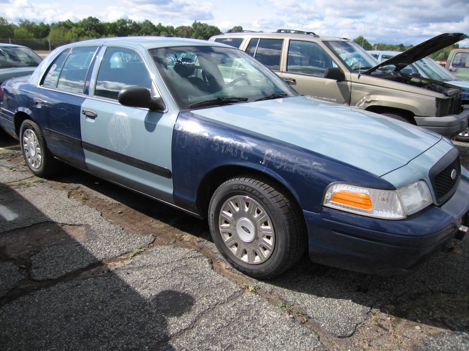 Two-tone blue Ford Crown Victoria parked next to a tan SUV with its hood up