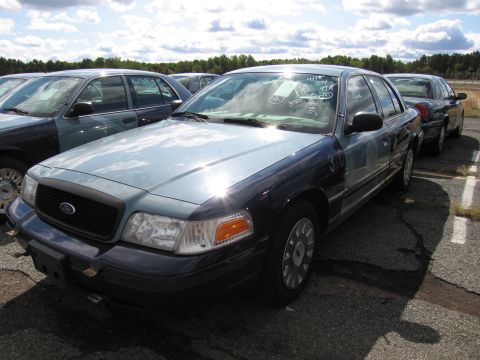 1991 Ford LTD Crown Victoria - A light blue and dark blue Ford Crown Victoria sedan is parked in a lot with other vehicles under a cloudy sky.