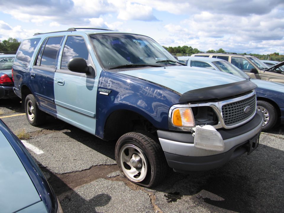 Two-tone blue SUV with flat tire and missing headlight, marked "115 EXPEDITION"