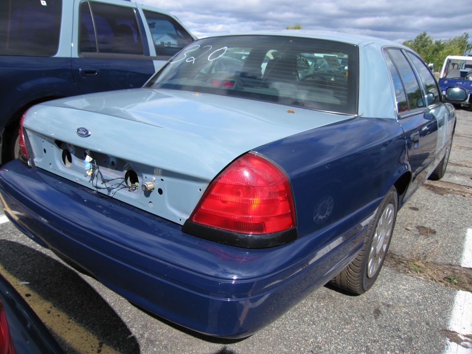 Rear of a blue and light blue Ford Crown Victoria. License plate area is open. Another vehicle is parked behind it