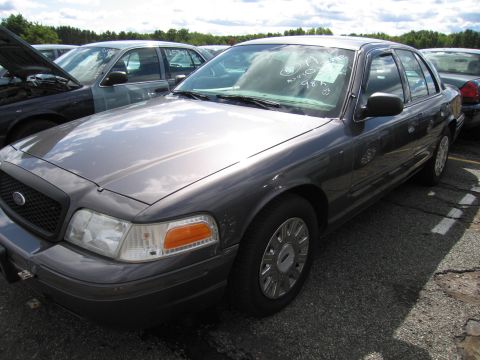 1991 Ford LTD Crown Victoria - A dark gray Ford Crown Victoria sedan is parked in a lot with other vehicles, showing its front quarter view.