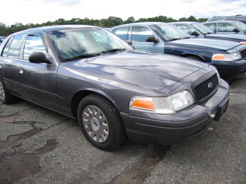 1991 Ford LTD Crown Victoria - A row of Ford Crown Victorias are parked on a gravel lot under a cloudy sky.