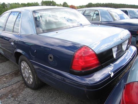 1991 Ford LTD Crown Victoria - A blue and light blue sedan is parked in a lot with other vehicles, showing writing on its rear window.