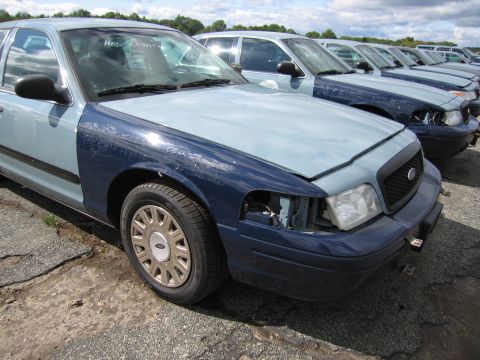 1991 Ford LTD Crown Victoria - A row of Ford Crown Victorias, one with two-tone paint and damage, sits in a junkyard.