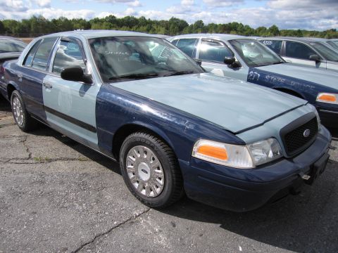 1991 Ford LTD Crown Victoria - A two-tone police car, likely a 1991 Ford Crown Victoria LTD, is parked in a lot with other vehicles. Text on the windshield reads 'STRIPPE…