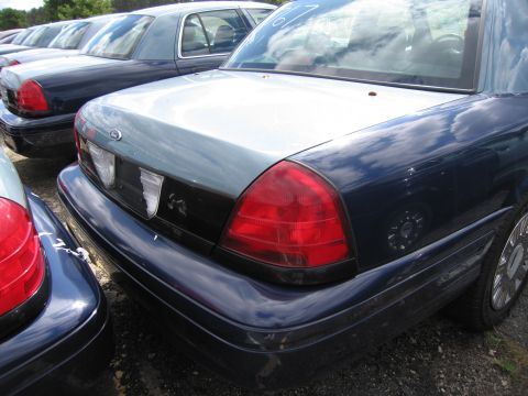 1991 Ford LTD Crown Victoria - A line of dark blue Ford Crown Victorias are parked outdoors, showing their rear ends.