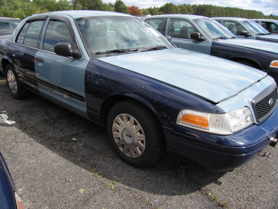 Two-tone Ford Crown Victoria with light blue hood and front fender, dark blue doors and rear fender, parked in lot with other similar vehicles
