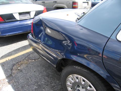 1991 Ford LTD Crown Victoria - This dark blue sedan shows extensive damage to its rear quarter panel, with another vehicle visible behind it.