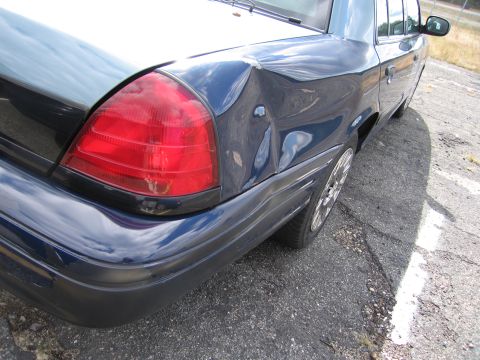 1991 Ford LTD Crown Victoria - Rear view of a dark blue sedan showing significant damage to the rear quarter panel.
