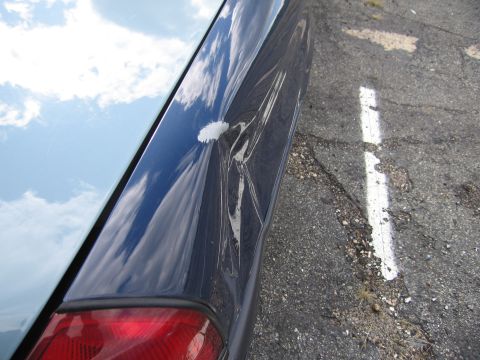 1991 Ford LTD Crown Victoria - A dent and scrape are visible on the side of a dark blue vehicle, with clouds reflected in the undamaged portion.